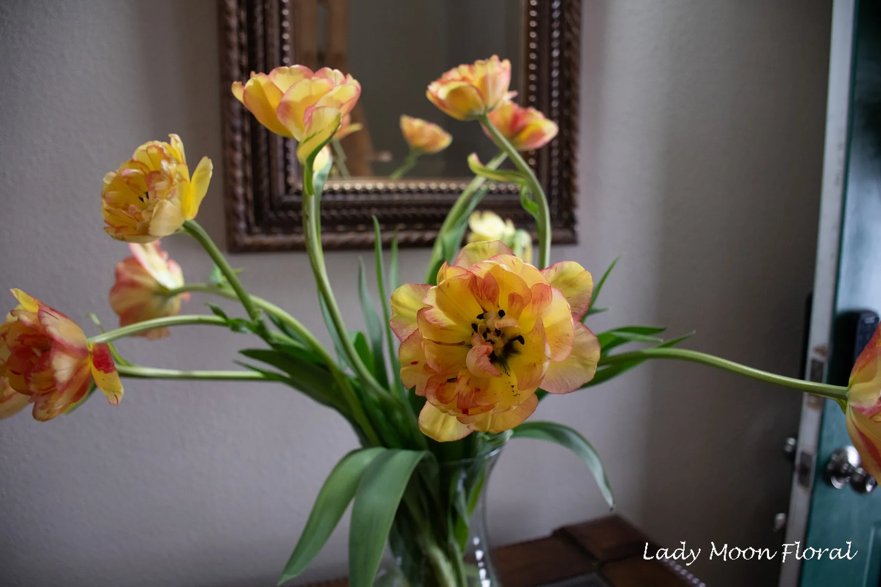 Yellow-orange tulips in vase with mirror reflection