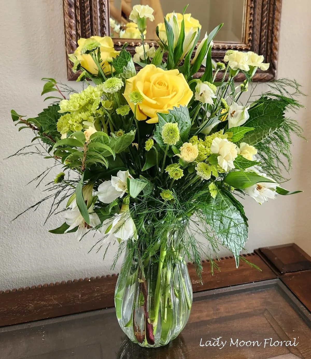 Yellow roses in glass vase on wooden table.